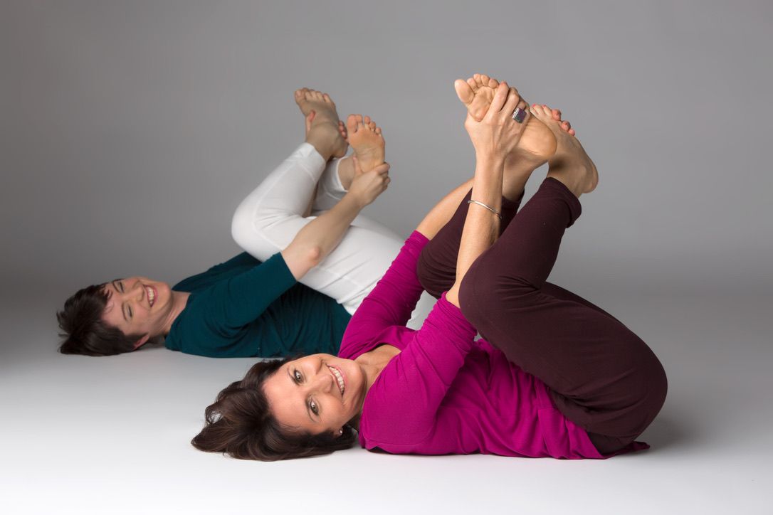 Deux femmes allongées sur le dos, tenant leurs pieds, pendant un atelier